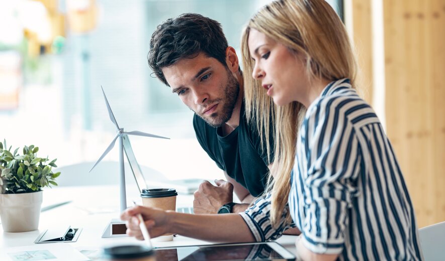 Zwei Personen besprechen nachhaltige Projekte und arbeiten gemeinsam an einem Tisch mit Windradmodell